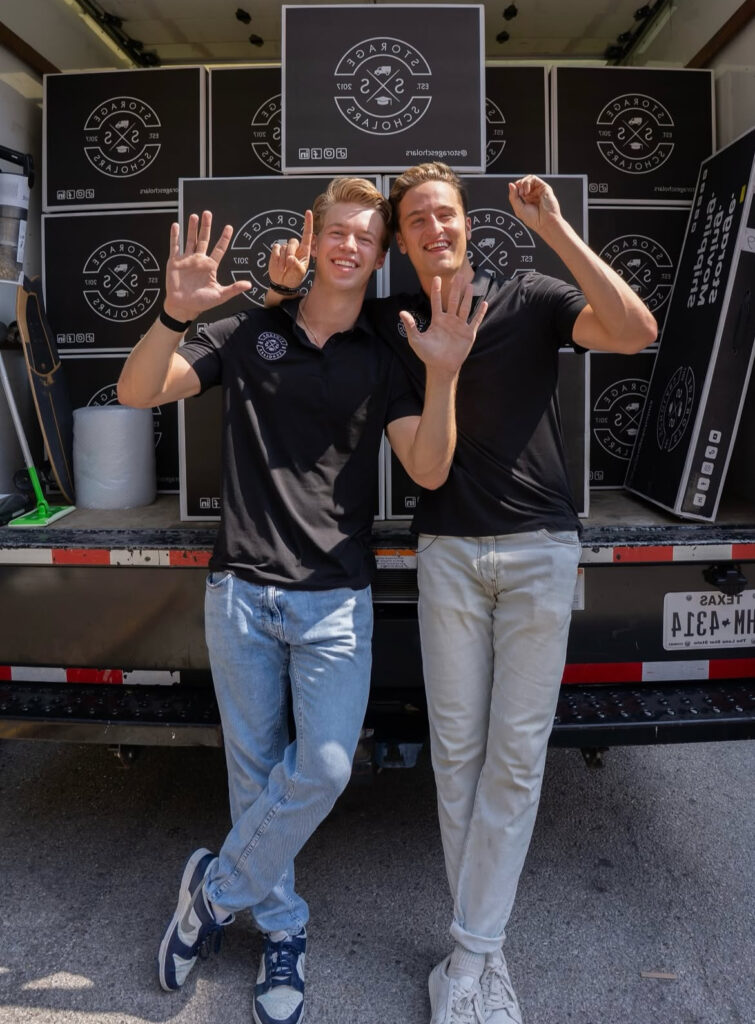 Two Storage Scholars co-founders celebrating in front of a loaded branded moving truck, both raising their hands with five fingers spread